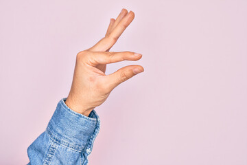 Hand of caucasian young man showing fingers over isolated pink background picking and taking invisible thing, holding object with fingers showing space