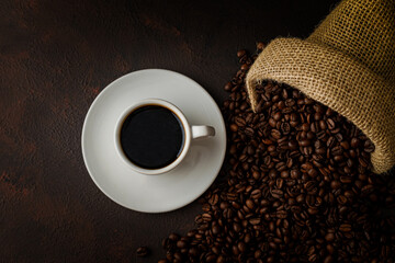 Top view of a Cup of coffee with beans on brown rustic table and black background