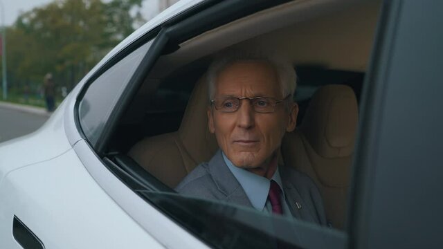old businessman rides in the back seat of a car