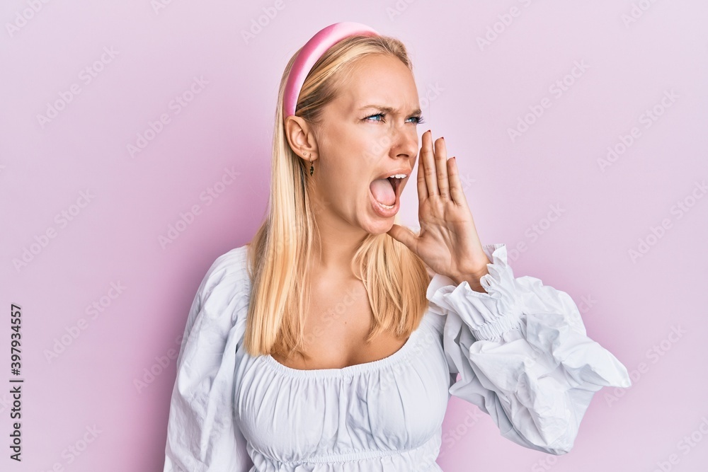 Poster Young blonde girl wearing casual clothes shouting and screaming loud to side with hand on mouth. communication concept.