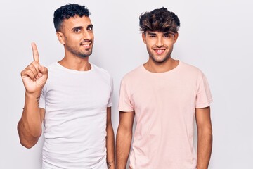 Young gay couple wearing casual clothes showing and pointing up with finger number one while smiling confident and happy.