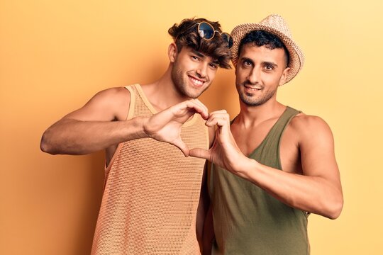 Young gay couple wearing summer clothes smiling in love doing heart symbol shape with hands. romantic concept.