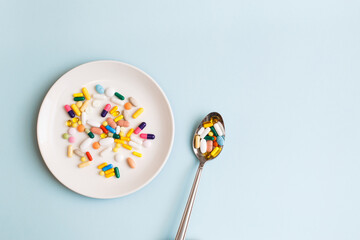 Creative medical layout made with colorful pills, capsules and supplements on white plate on light blue background. Minimal modern pharmacy or health care concept. Flat lay, top view, copy space