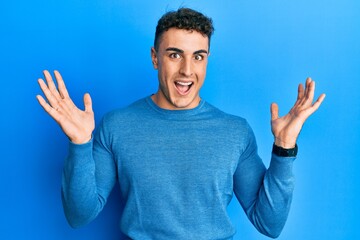 Naklejka premium Hispanic young man wearing casual winter sweater celebrating crazy and amazed for success with arms raised and open eyes screaming excited. winner concept