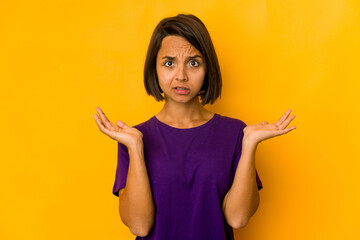 Young hispanic woman isolated on yellow doubting and shrugging shoulders in questioning gesture.