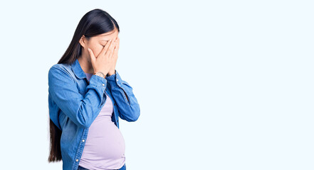 Young beautiful chinese woman pregnant expecting baby with sad expression covering face with hands while crying. depression concept.