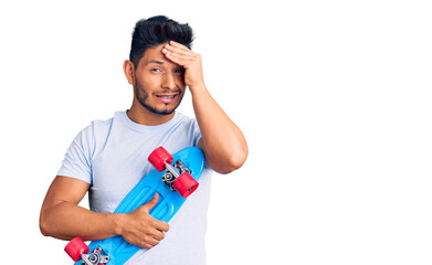 Handsome latin american young man holding skate stressed and frustrated with hand on head, surprised and angry face