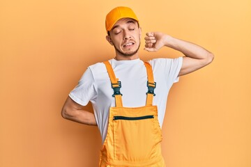 Hispanic young man wearing handyman uniform stretching back, tired and relaxed, sleepy and yawning for early morning