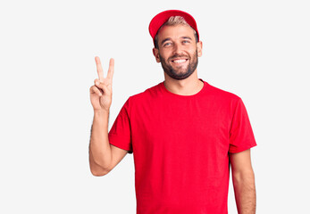 Naklejka premium Young handsome blond man wearing t-shirt and cap showing and pointing up with fingers number two while smiling confident and happy.