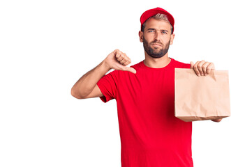 Young handsome blond man holding delivery paper bag with angry face, negative sign showing dislike with thumbs down, rejection concept