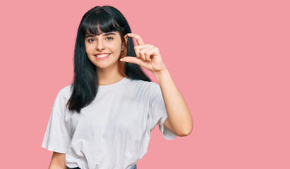 Young hispanic girl wearing casual clothes smiling and confident gesturing with hand doing small size sign with fingers looking and the camera. measure concept.