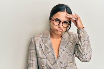 Young brunette woman wearing business jacket and glasses worried and stressed about a problem with hand on forehead, nervous and anxious for crisis