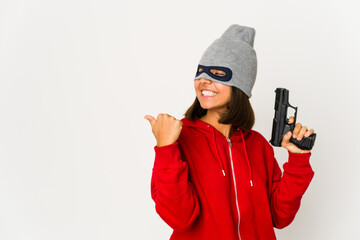 Young robber hispanic woman wearing a mask points with thumb finger away, laughing and carefree.