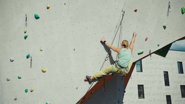 Young woman rock climber climbing on artificial rock wall in outside climbing gym. sports woman working out on extrime sport route. strength, conquering and training concept