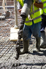 Worker filling the foundation slab of a building under construction with a pipe from which cement