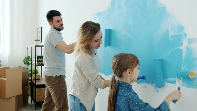 Cheerful family mother fether and child are painting wall and dancing enjoying music at home during renovation. Domestic activities and people concept.