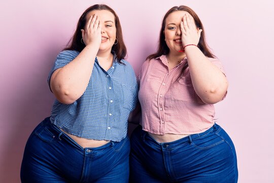 Young plus size twins wearing casual clothes covering one eye with hand, confident smile on face and surprise emotion.
