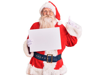 Naklejka premium Old senior man with grey hair and long beard wearing santa claus costume holding banner surprised with an idea or question pointing finger with happy face, number one
