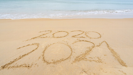 Fototapeta na wymiar Photo of coming New Year 2021 Text and leaving year of 2020 of lettering Text on the beach with wave and white sea foam Numbers 2021 year on the seashore wave crashing on sandy shore