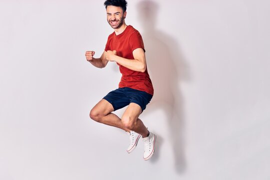 Young handsome man wearing casual clothes smiling happy. Jumping with smile on face doing winner gesture with fists up over isolated white background