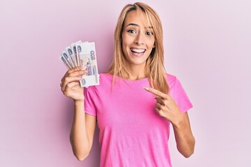 Beautiful blonde woman holding 500 russian ruble banknotes smiling happy pointing with hand and finger
