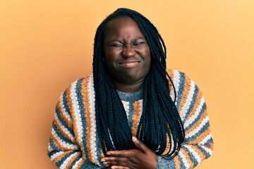 Young black woman with braids wearing casual winter sweater with hand on stomach because indigestion, painful illness feeling unwell. ache concept.