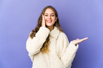 Young caucasian cute woman holds copy space on a palm, keep hand over cheek. Amazed and delighted.