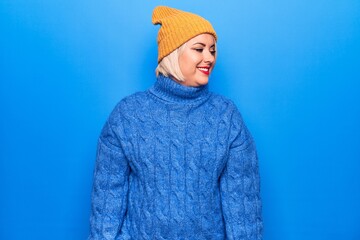 Young beautiful blonde plus size woman wearing blue casual turtleneck sweater and wool hat looking to side, relax profile pose with natural face and confident smile.