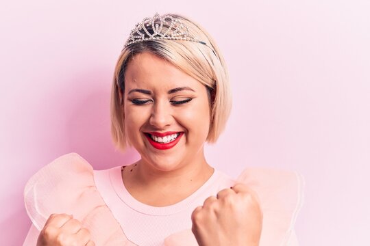 Beautiful blonde plus size woman wearing pincess tiara with diamonds over pink background celebrating surprised and amazed for success with arms raised and eyes closed