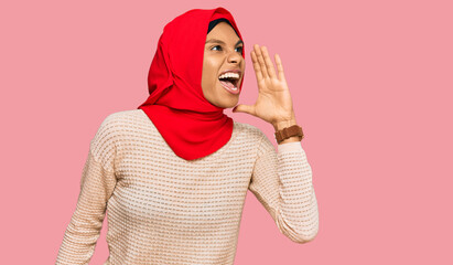 Obraz premium Young african american woman wearing traditional islamic hijab scarf shouting and screaming loud to side with hand on mouth. communication concept.