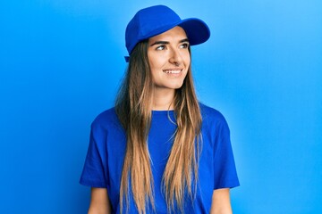 Naklejka premium Young hispanic woman wearing delivery uniform and cap looking away to side with smile on face, natural expression. laughing confident.