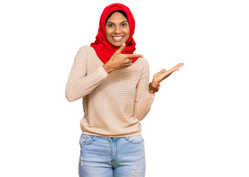 Young african american woman wearing traditional islamic hijab scarf amazed and smiling to the camera while presenting with hand and pointing with finger.