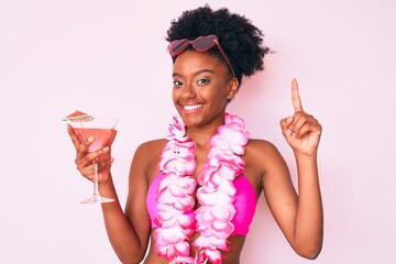 Young african american woman wearing bikini and hawaiian lei holding cocktail surprised with an...