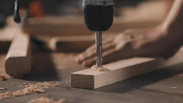 Closeup of unrecognizable strong male hands screwing into piece of wood making diy furniture in carpentry