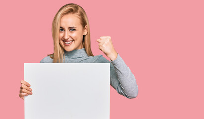 Fototapeta premium Beautiful caucasian woman holding blank empty banner screaming proud, celebrating victory and success very excited with raised arms