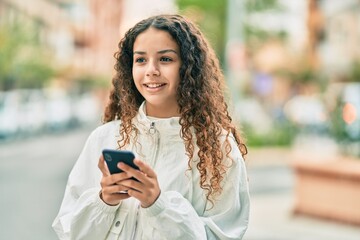 Beautiful hispanic girl smiling happy using smartphone at the city.