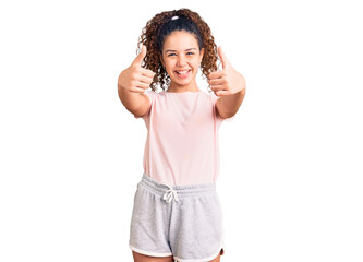 Beautiful kid girl with curly hair wearing casual clothes approving doing positive gesture with hand, thumbs up smiling and happy for success. winner gesture.