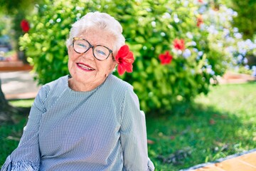Elder senior woman with grey hair smiling happy outdoors wearing a decorative flower
