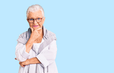 Senior beautiful woman with blue eyes and grey hair wearing casual clothes and glasses looking confident at the camera smiling with crossed arms and hand raised on chin. thinking positive.