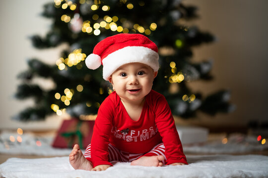 adorable little baby boy in a santa costume sitting on a soft fake fur in front of a christmas tree