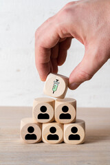 hand placing a cube with a syringe symbol on top of stacked cubes with person symbols on wooden...