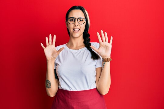 Young hispanic woman wearing professional waitress apron afraid and terrified with fear expression stop gesture with hands, shouting in shock. panic concept.