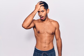 Young latin man standing shirtless surprised with hand on head for mistake, remember error. forgot, bad memory concept.