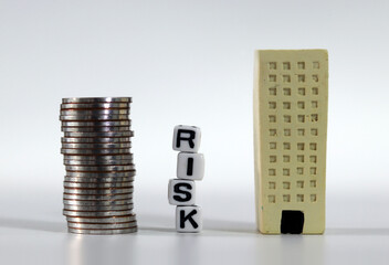 Risk management concept. White cubes with RISK word and miniature building and a pile of coins.
