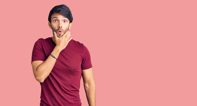 Handsome hispanic man wearing casual clothes looking fascinated with disbelief, surprise and amazed expression with hands on chin