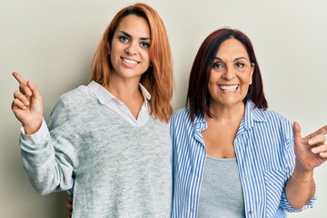 Latin mother and daughter wearing casual clothes smiling happy pointing with hand and finger to the side