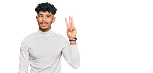 Fototapeta premium Young arab man wearing casual winter sweater showing and pointing up with fingers number three while smiling confident and happy.