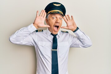 Handsome middle age mature man wearing airplane pilot uniform smiling cheerful playing peek a boo with hands showing face. surprised and exited