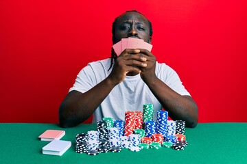 Handsome young black man playing gambling poker covering face with cards looking at the camera blowing a kiss being lovely and sexy. love expression.