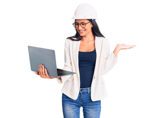 Young beautiful latin girl wearing architect hardhat holding laptop celebrating victory with happy smile and winner expression with raised hands